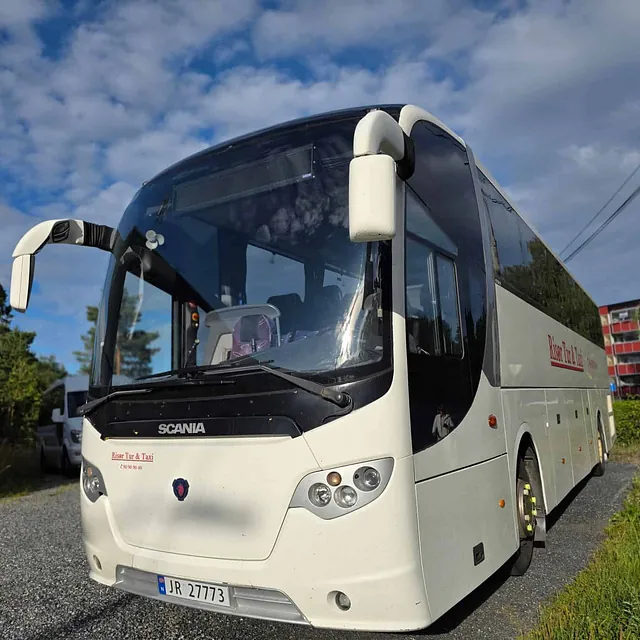 Hvit turbuss fra Risør Tur & Taxi parkert på grusvei under blå himmel.